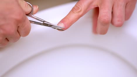 manicure, cutting fingernails with nail scissors over toilet