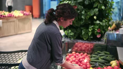 Junge-Schöne-Brünette-Mädchen-In-Den-Zwanzigern,-Die-Am-Obst--Und-Gemüsegang-Eines-Lebensmittelgeschäfts-Tomaten-In-Eine-Plastiktüte-Aussortiert