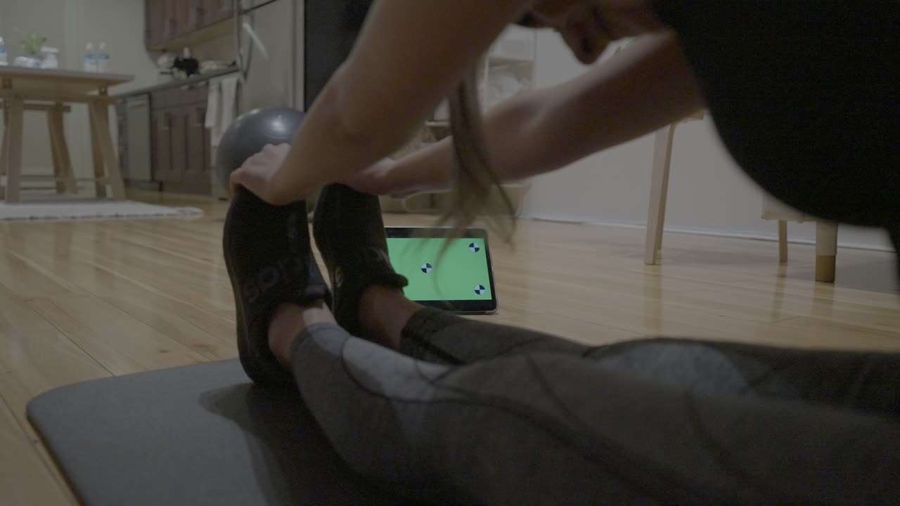una toma estática de una mujer hispana estirándose mientras mira y habla con una tableta verde en la sala de estar de su casa