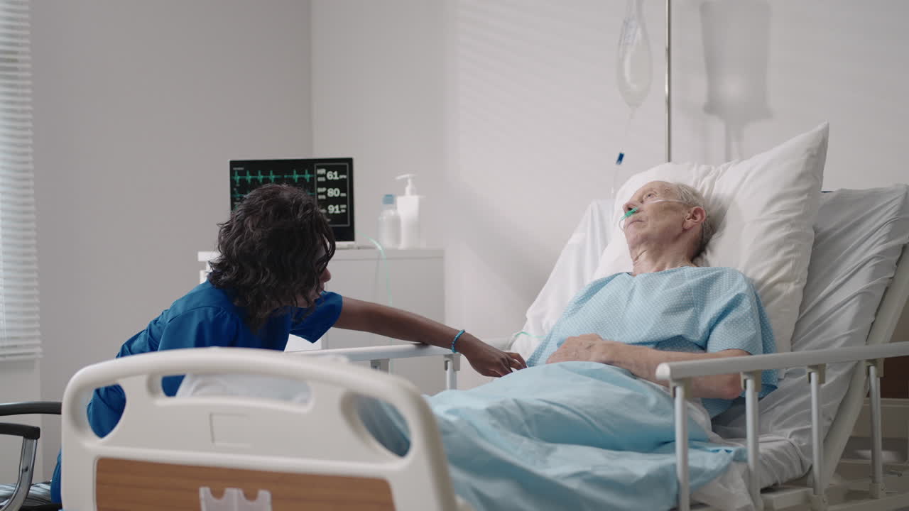 una doctora de piel oscura está hablando con un anciano paciente de sexo masculino acostado en una cama de hospital discutiendo la rehabilitación después de la recuperación.
