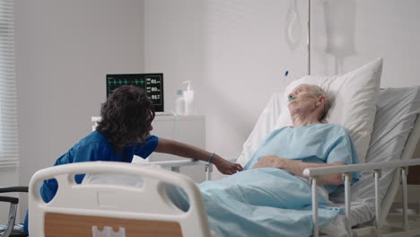 a dark-skinned female doctor is talking to an old male patient lying on a hospital bed discussing rehabilitation after recovery.