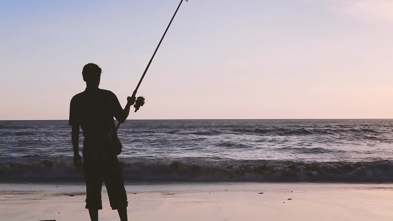 Silhouette di alta qualità di un uomo con canna da pesca sulla spiaggia di Bali al tramonto. Cielo al tramonto con spazio libero.
