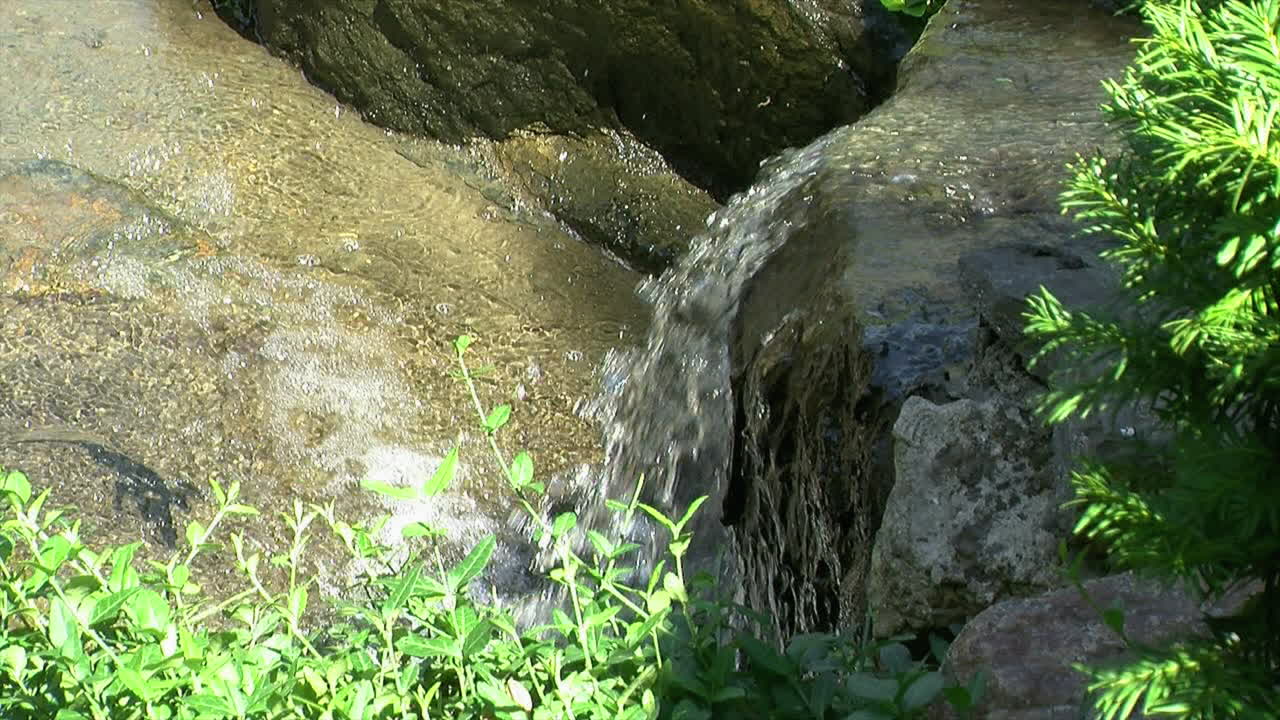 Cascade of water flows over the brink of a small waterfall, then downstream