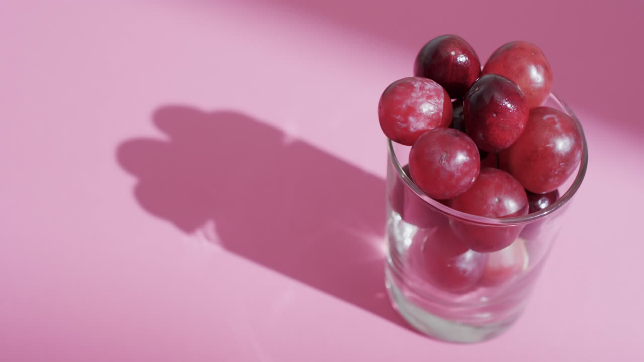 video de uvas rojas en vidrio con espacio de copia en fondo rosa