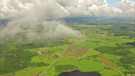 drone aéreo disparado a través de las nubes sobre el campo rural verde junto a un lago en una mañana soleada