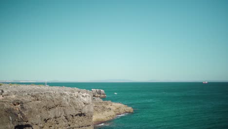 Vista-Pacífica-De-La-Costa-Del-Océano-Con-Acantilado-Rocoso,-Olas-Rompiendo-Y-Cielo-Azul-En-Cascais-Portugal-4k-Jib-Shot