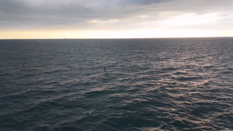 Surfista-Solitario-En-El-Vasto-Océano-Con-Un-Barco-Distante,-Cielos-Nublados-Sobre-Génova,-Italia,-Puesta-De-Sol-En-El-Horizonte