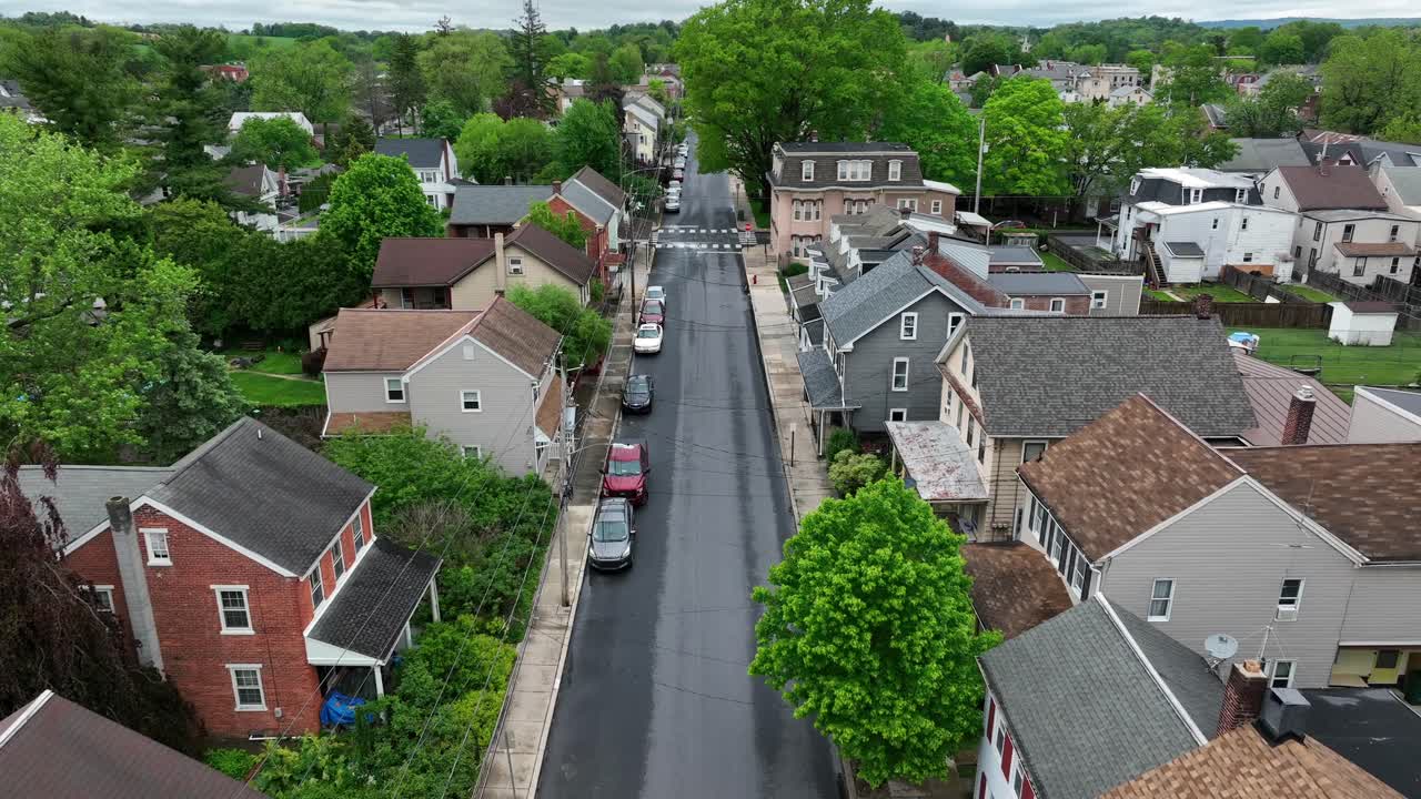 Black car crossing junction of quiet american neighborhood with row of houses in classical style. Geren trees in spring. American city neighborhood with townhouses and historic row homes.
