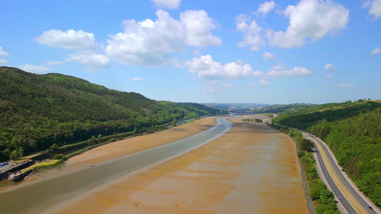 Low, rising aerial video of the Newry River and Mourne Mountains in Warrenpoint, County Down, Northern Ireland, UK on a bright and sunny day. Filmed in 4K, 60FPS and with Rec709 color.