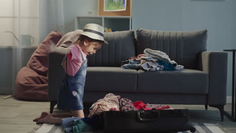 girl puts clothes pile into suitcase and imitates airplane