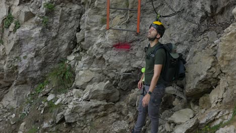 a man prepares to record himself with a drone on a rocky mountain trail, equipped with safety gear and a helmet. the scene highlights adventure, self-filming, and outdoor exploration