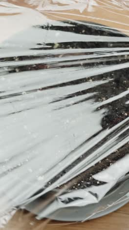 close-up vertical video of covering potting soil with plastic wrap. home gardening. eco living.