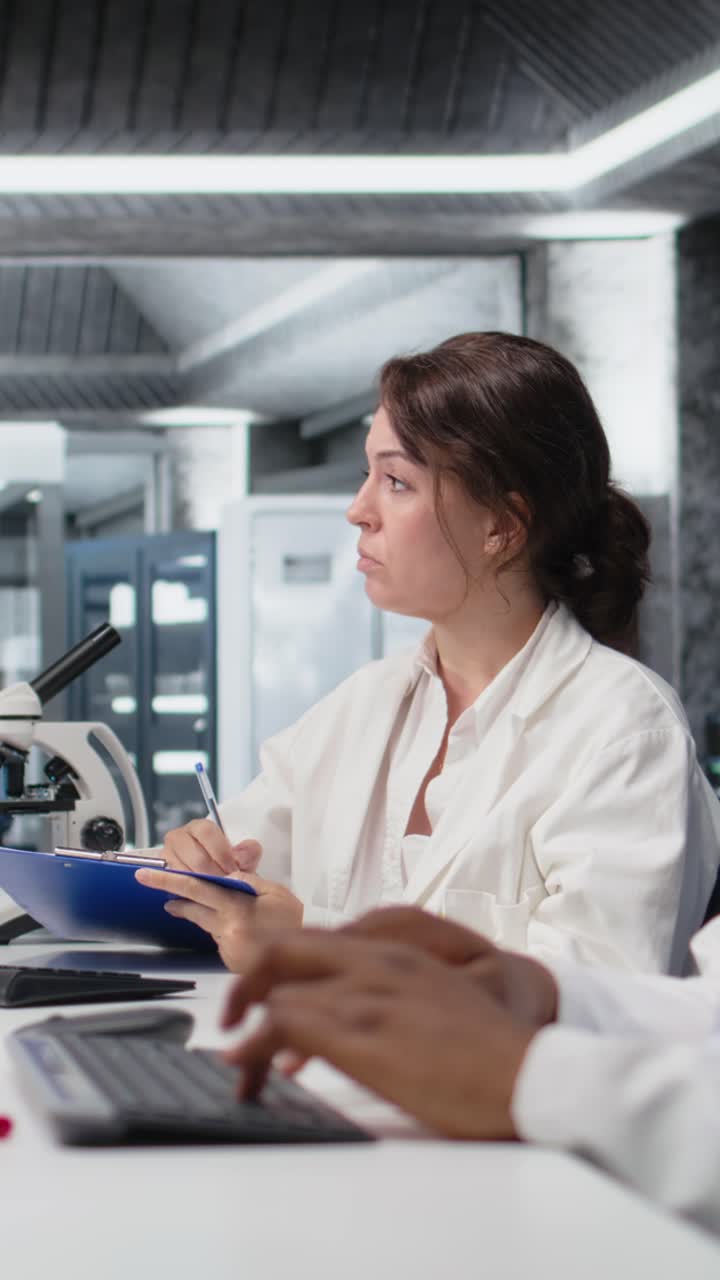 Vídeo vertical de um(a) tecnólogo(a) de laboratório clínico fazendo anotações sobre um experimento laboratorial