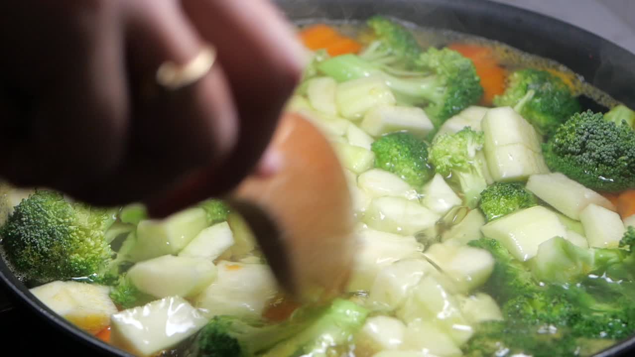Primo piano di una mano che mescola verdure fresche che cuociono in una pentola