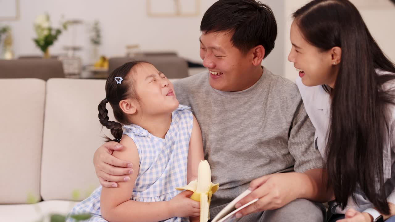 A joyful family shares a moment on the couch, enjoying bananas together in a bright, cozy living room