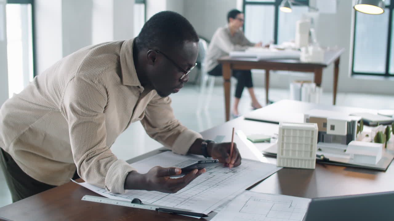 Black Male Architect Using Smartphone and Drawing Floor Plan