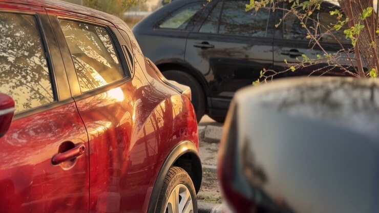 Un'auto rossa parcheggiata all'aperto accanto a un SUV nero durante l'ora d'oro. La calda luce del tramonto si riflette sul finestrino laterale del veicolo e sulla vernice lucida in questa vista con profondità di campo ridotta