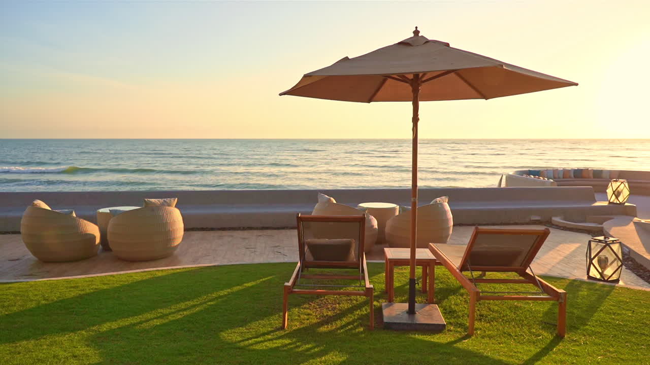 Wide, relaxing shot of luxury sun beds overlooking ocean sunrise, green grass