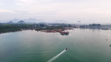 Long-tail-boat-sailing-towards-jetty-on-hazy-ocean-coast-of-Thailand