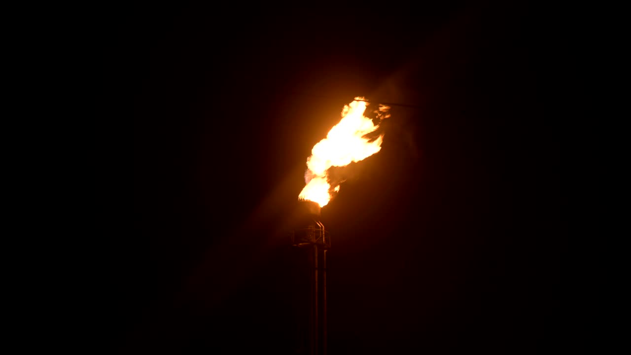 una toma nocturna de una antorcha de gas en llamas de la producción petroquímica en completa oscuridad. combustión de petróleo de baja clave y contaminación ambiental. concepto de problemas ecológicos