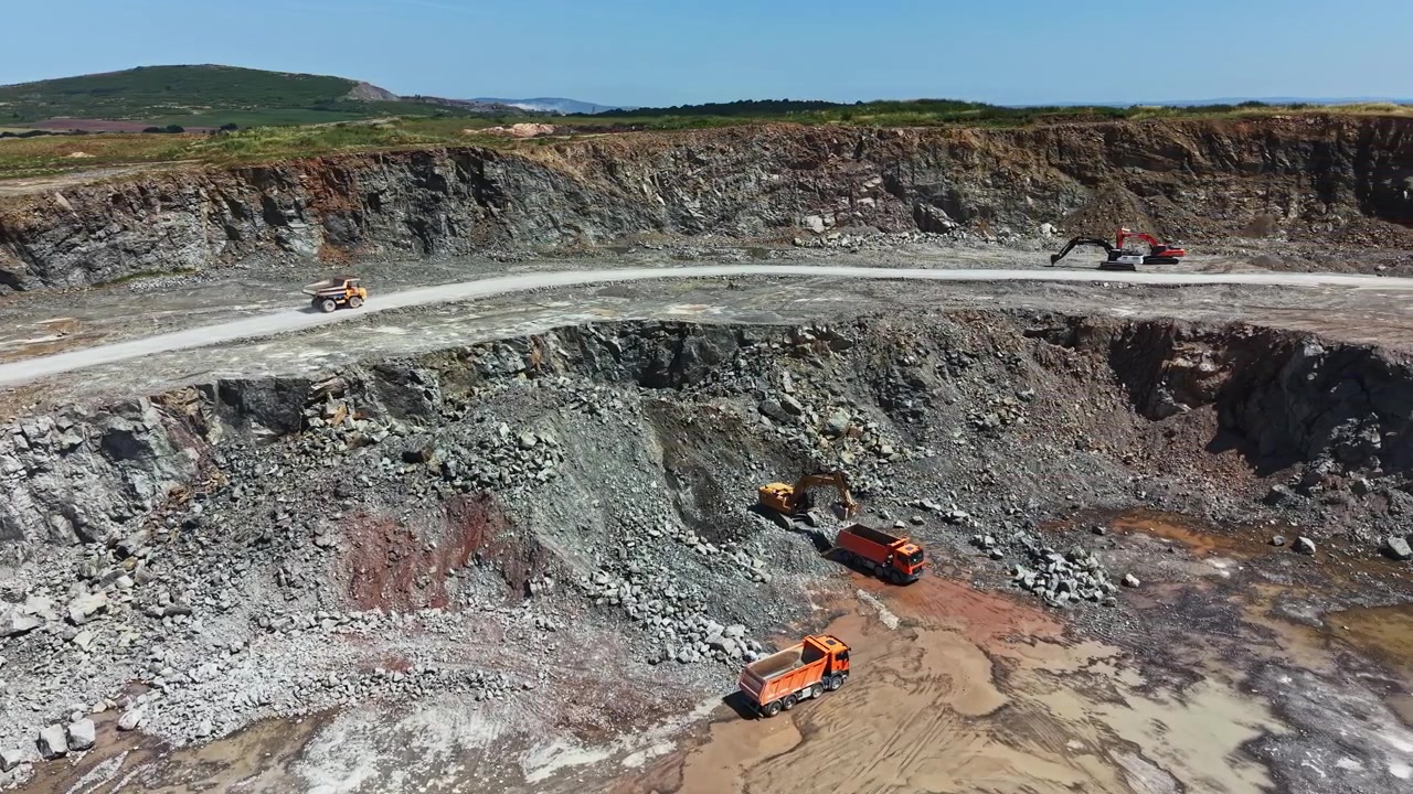 Granite quarry operation during daylight with machinery and trucks engaged in mineral extraction and site preparation
