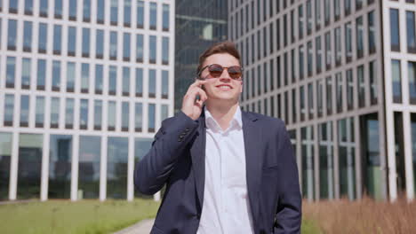 A-young-happy-entrepreneur-walks-and-talks-on-the-phone-in-front-of-a-modern-office-building