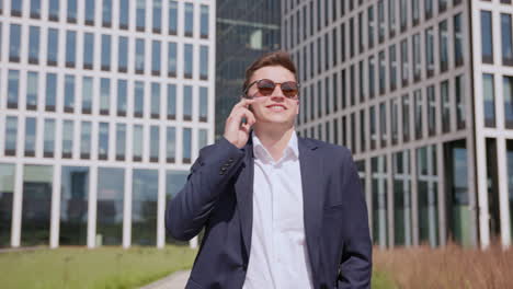 a young happy entrepreneur walks and talks on the phone in front of a modern office building