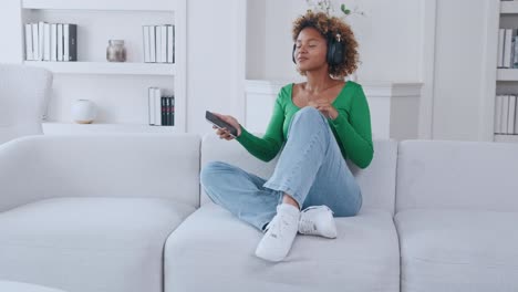 young carefree african american woman dances sits on sofa and closing eyes