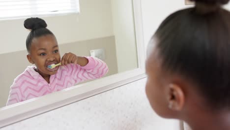 feliz chica afroamericana inalterada cepillándose los dientes en el baño, en cámara lenta