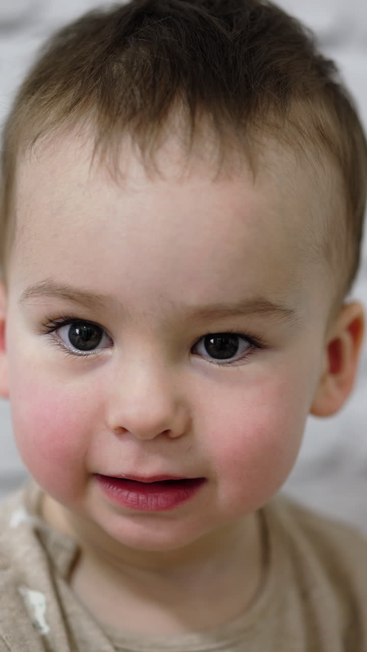 Charming little Caucasian boy smiling adorably to the camera. Close up portrait of a one year toddler. Vertical video