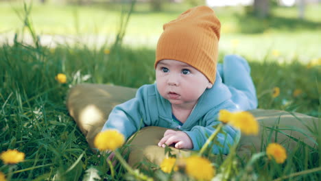 cute toddler lying on the mattress in the grass with dandelions. adorable baby looks up smiling sweetly.