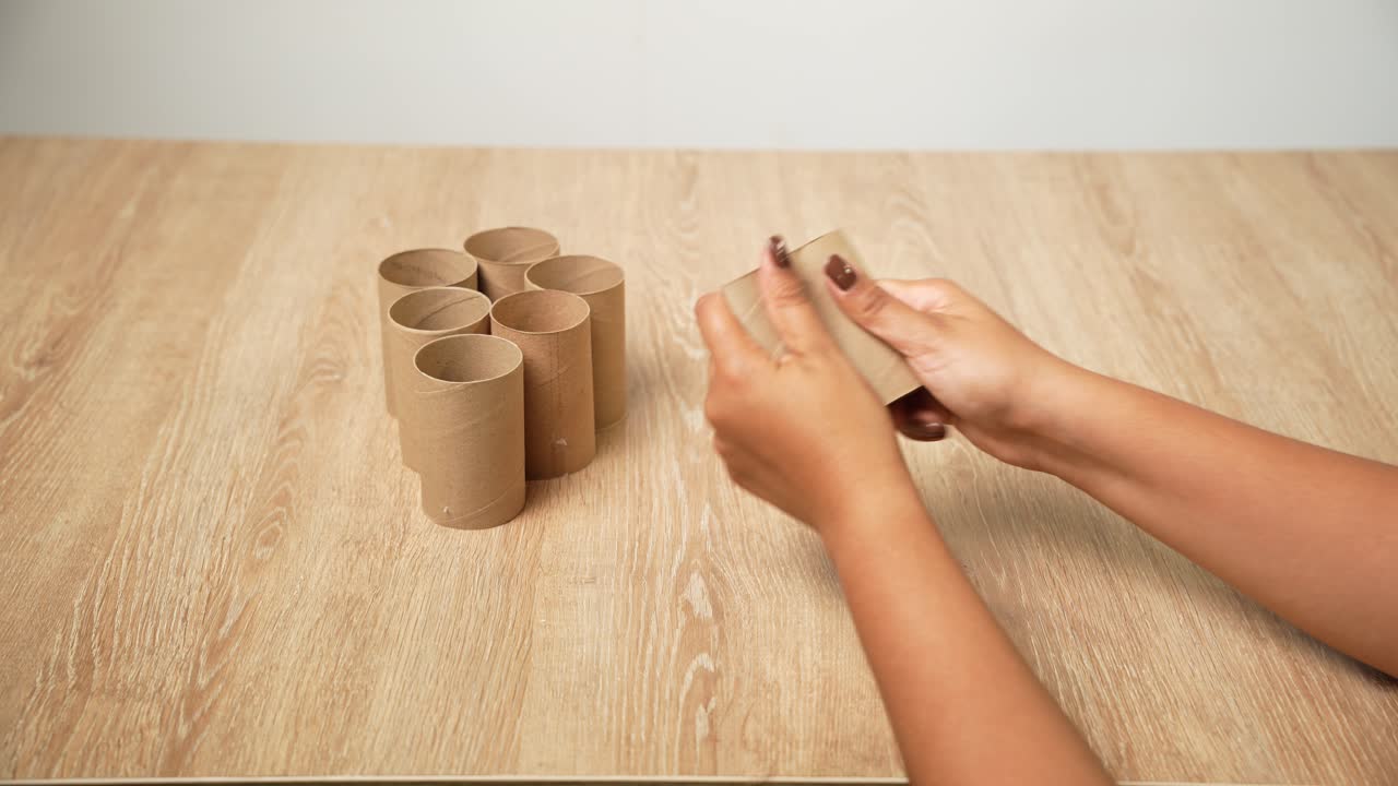 Filmagem em close-up de mãos arrumando pequenos rolos de papel e cortando uma peça para iniciar um projeto de artesanato. O vídeo mostra o processo de preparação e o trabalho manual cuidadoso em um espaço de trabalho criativo.