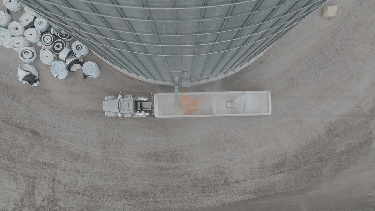 Aerial top shot of semi loading corn at farmstead grain bin through trucks.