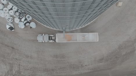 aerial top shot of semi loading corn at farmstead grain bin through trucks.