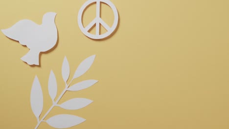 close up of white dove with peace sign and leaf and copy space on yellow background