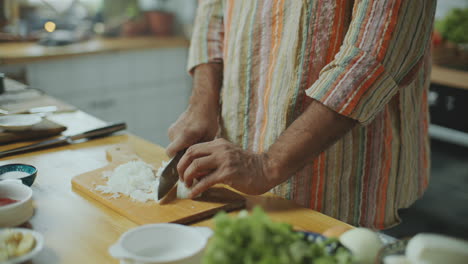 close-up of hands of chef chopping onion on wooden cutting board