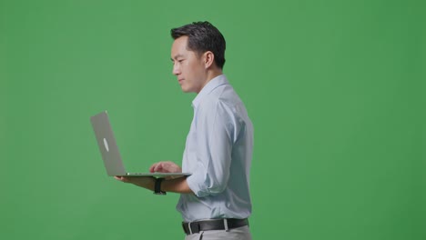스튜디오에서 녹색 화면 배경에서 는 동안 노트북 컴퓨터를 사용하는 아시아 사업가의 측면 시각