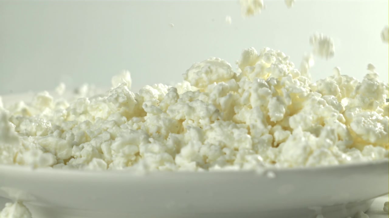 Hytteost falder ned på en hvid tallerken i slowmotion