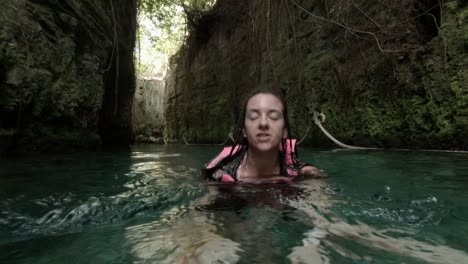 caucasian female talking while swimming in a blue river wearing a life jacket