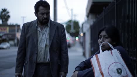 a poignant moment captures the emotional tension of a man approaching a contemplative woman sitting on the street, highlighting themes of isolation and societal struggles.