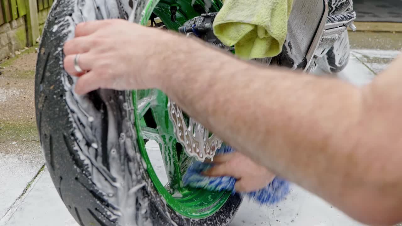 Cleaning rear motorbike green wheel with shampoo snow foam and blue wash mitt