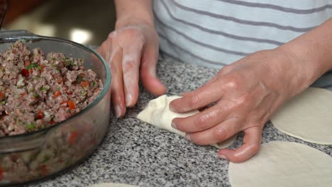 close-up of woman's hands making meat fatayers also known as middle eastern savory hand pies