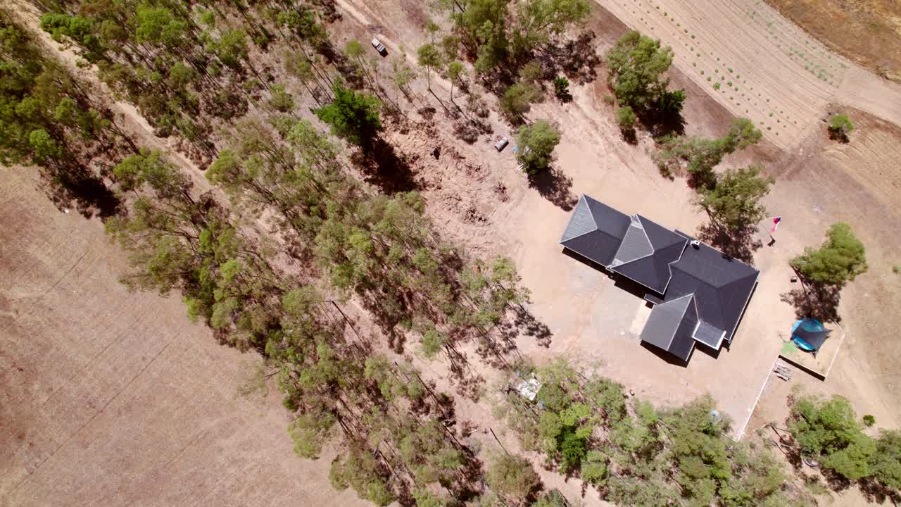 Fugleperspektiv af et ensomt landhus med gråt tag midt på en mark, nedadgående optagelse.