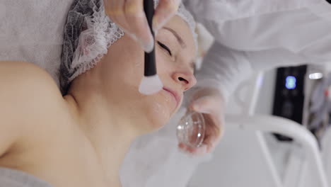 enzyme therapy beautician applying moisturizing medical cream on middleaged woman face with brushes