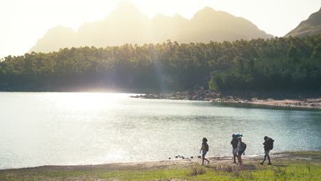 wide angle view of group of friends with backpacks on vacation hiking by lake and mountains