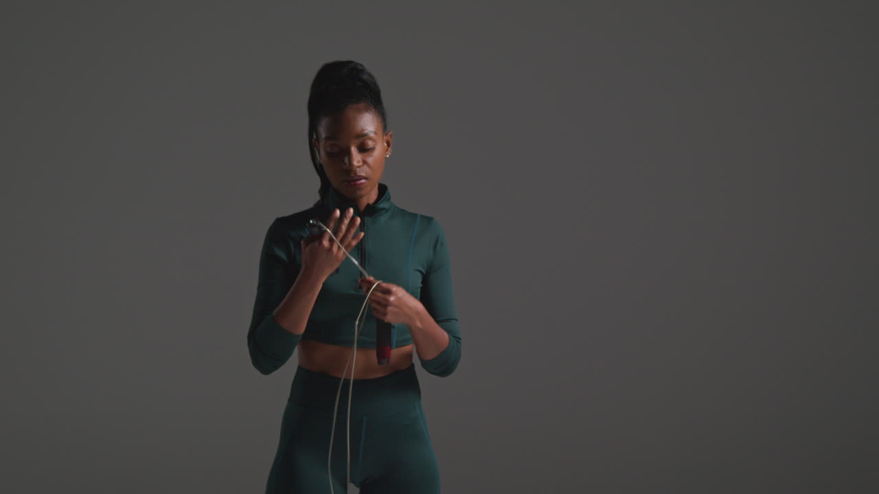 fotografía de cerca de una atleta que usa un traje de entrenamiento en una clase de gimnasia con cuerda de salto o cuerda de saltado contra un fondo plano