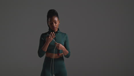 Close-Up-Shot-Of-Female-Athlete-Wearing-Tracksuit-Training-In-Gym-Fitness-Class-With-Jump-Rope-Or-Skipping-Rope-Against-Plain-Background