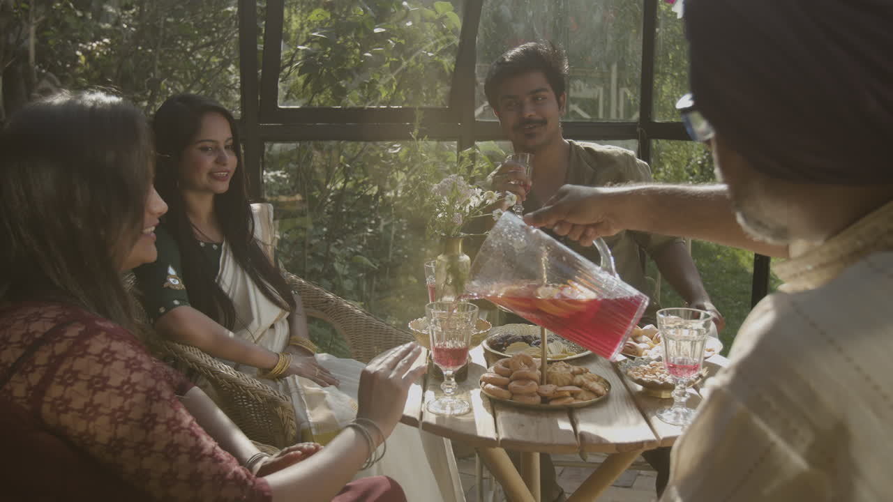 A group of people enjoying a social gathering with food and drinks in a sunny garden setting
