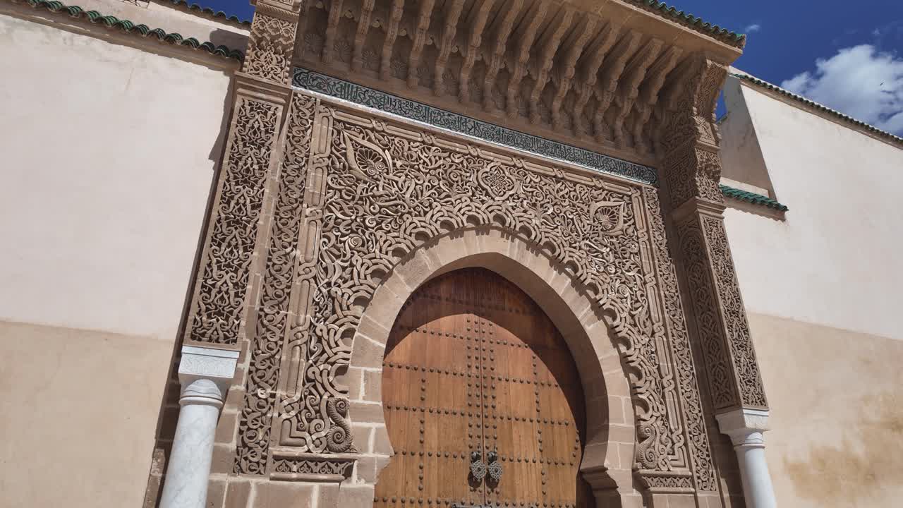 Ornate entrance of the Mausoleum of Moulay Ismail in Meknes, Morocco, showcasing detailed carvings and a large wooden door