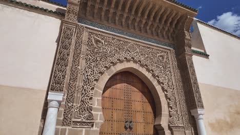 ornate entrance of the mausoleum of moulay ismail in meknes, morocco, showcasing detailed carvings and a large wooden door